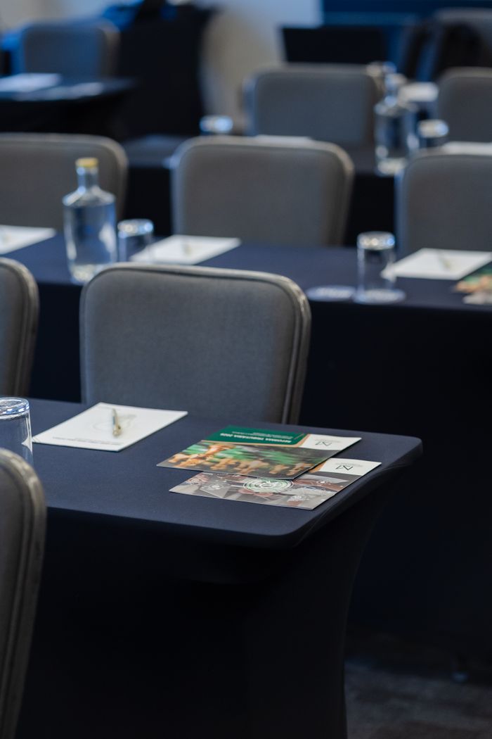 Elegant conference room setup with notepads, water bottles, and glasses on black cloth tables.